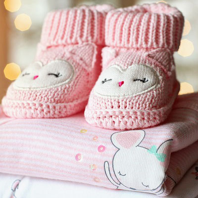 Pink baby booties and baby clothes. New baby messages for greeting cards.