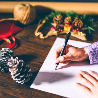 Christmas messages for friends writing in a Christmas card with black pen on desk with pine cones and Christmas decorations.